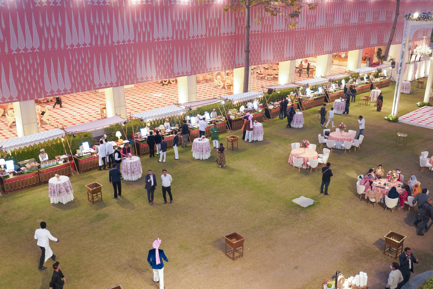 Aerial daytime view of Aarna Farms wedding lawn in Noida — round tables with pink linens, live food counters and covered pandal seating for a large Indian wedding reception