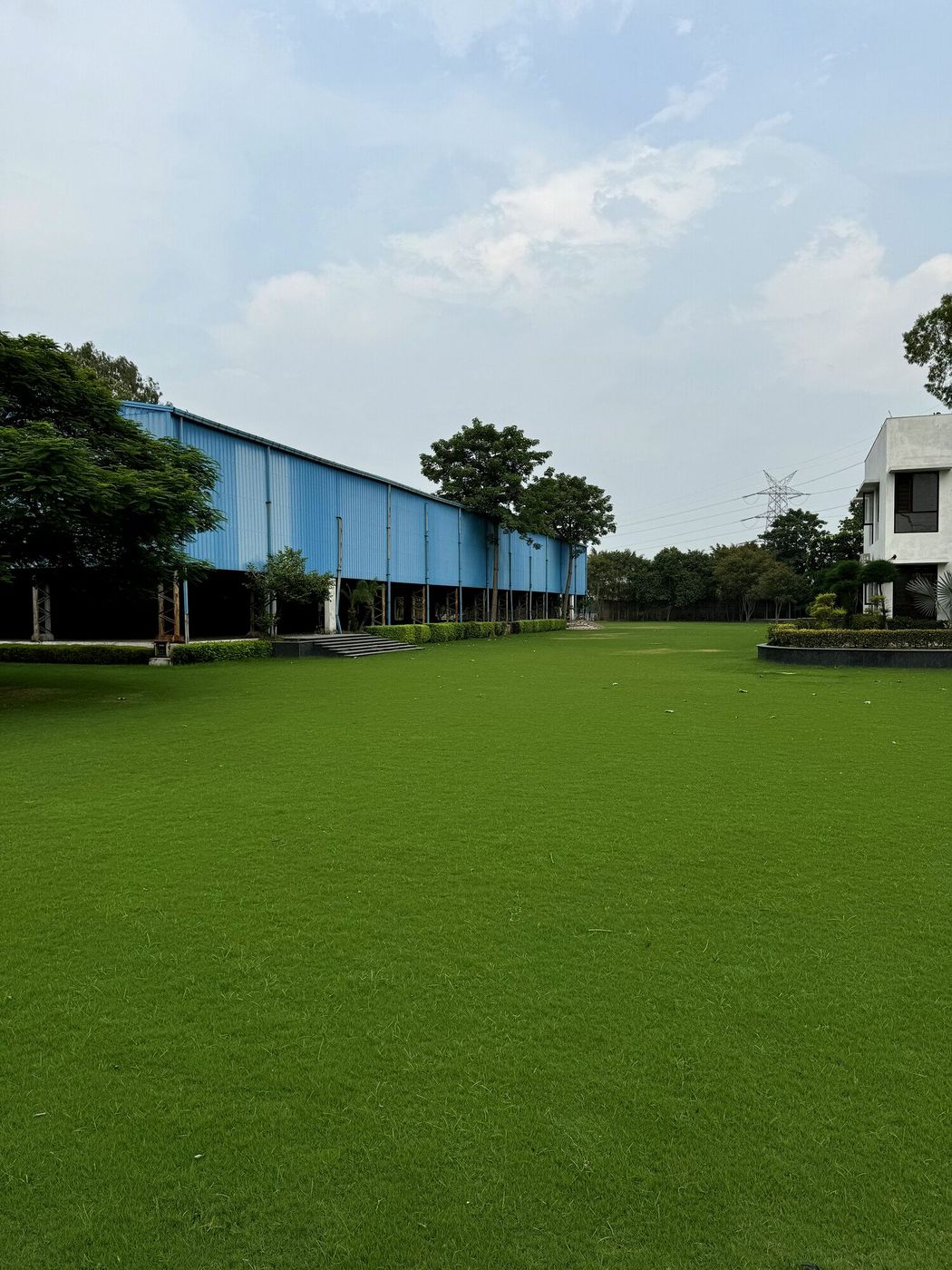 Empty open wedding lawn at Aarna Farms Sector-133 Noida — vast manicured green grass with covered pavilion and farmhouse, a blank canvas venue ready for wedding decor