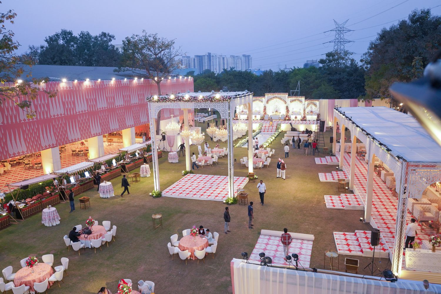 Ornate white wedding mandap with crystal chandeliers set up on Aarna Farms open lawn in Noida with pink pandal drapes and reception seating